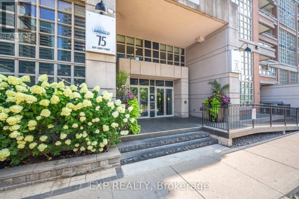 Building entrance with a concrete facade, glass doors, and landscaping featuring white hydrangeas. - 501 - 75 East Liberty Street, Toronto