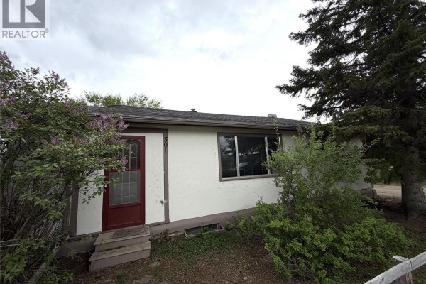 Exterior of a beige house with a red door and overgrown lilac bushes. - 501 Churchill Street, Hudson Bay