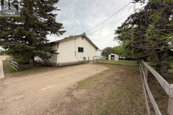Backyard view of a house with a gravel driveway and wooden fence. - 501 Churchill Street, Hudson Bay