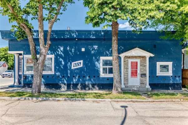 Side view of the blue duplex exterior with trees and a stone-accented entrance. - 501 Larsen Avenue, Winnipeg