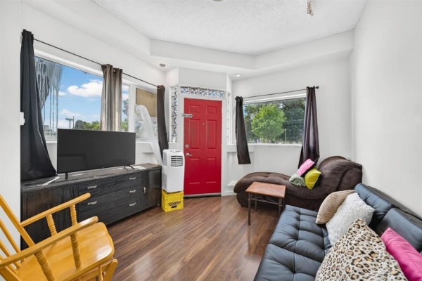 Living room with a black sectional sofa, wooden furniture, and a red front door. - 501 Larsen Avenue, Winnipeg