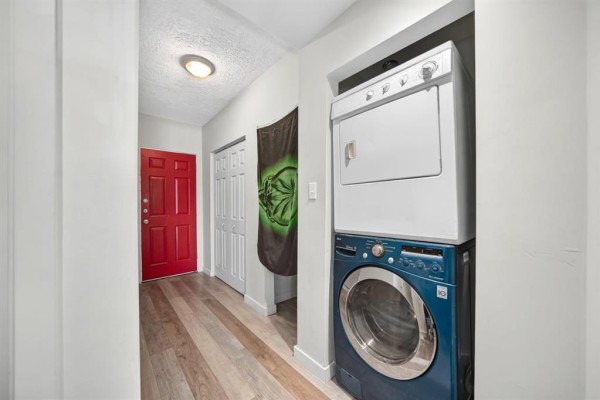 Hallway with a red door, white doors, and stacked washer and dryer units. - 501 Larsen Avenue, Winnipeg