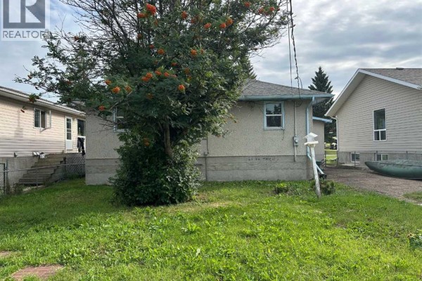 Side exterior of the house with a grassy yard and a large tree with orange berries. - 5010 44 Avenue, Ponoka