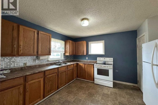 Kitchen with dark blue walls, oak cabinets, a double sink, and a white stove. - 5010 44 Avenue, Ponoka