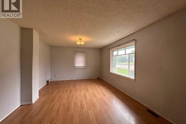 Living room with light wood laminate flooring, light grey walls, and a large window. - 5010 44 Avenue, Ponoka