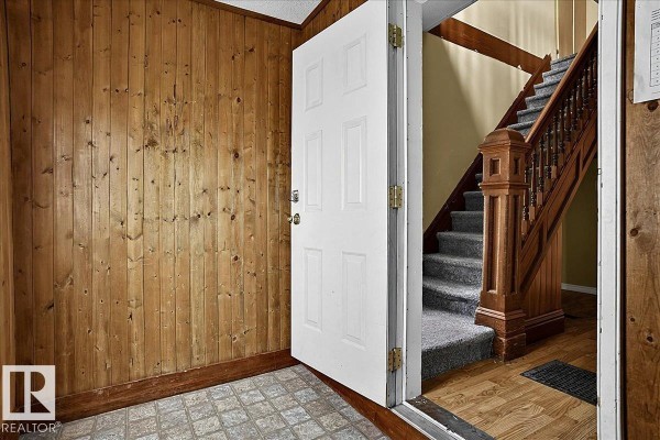 Interior entryway with wood-paneled walls, beige door, and carpeted staircase with wooden banister. - 5010 52 Av Nw, Wetaskiwin