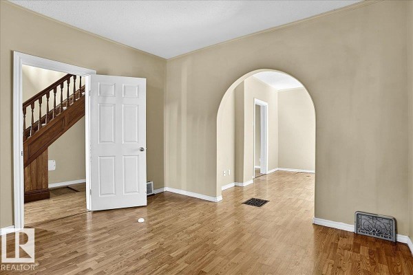 Living room with beige walls, hardwood floors, an arched doorway, and a view of the staircase. - 5010 52 Av Nw, Wetaskiwin