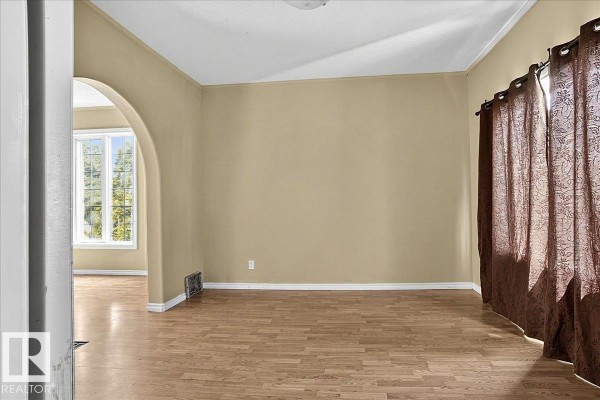 Living room with beige walls, hardwood floors, arched doorway, and brown patterned curtains on the right. - 5010 52 Av Nw, Wetaskiwin
