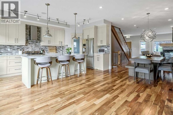 Open-concept kitchen with island, dining area, and stairs with wood floors. - 5013 23 Avenue Nw, Calgary