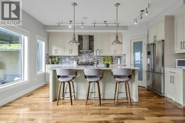 Kitchen with island, light beige cabinets, stainless steel appliances, and wood floors. - 5013 23 Avenue Nw, Calgary
