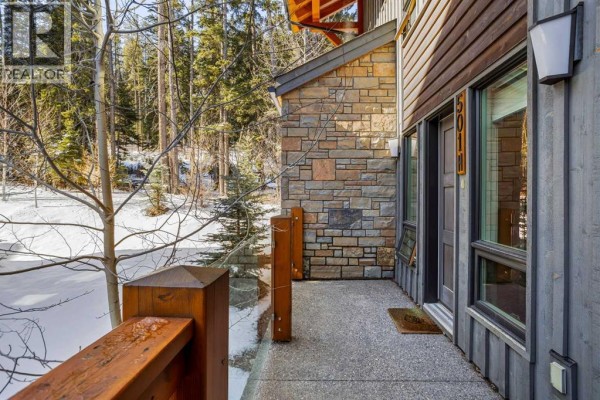Patio area with stone flooring and wooden railing, overlooking snowy landscape - 501h, 3000 Stewart Creek Drive, Canmore
