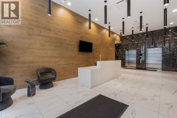 Building lobby with a white reception desk, modern chairs, and elevator doors. - 502, 110 18a Street Nw, Calgary
