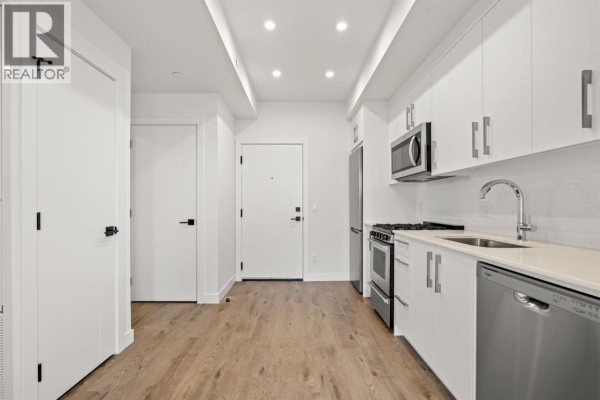 Compact kitchen with white cabinets, stainless steel appliances, and wood-look flooring. - 502, 110 18a Street Nw, Calgary