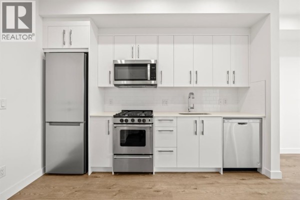 Apartment kitchen featuring white cabinets, stainless steel appliances, and light wood floors. - 502, 110 18a Street Nw, Calgary