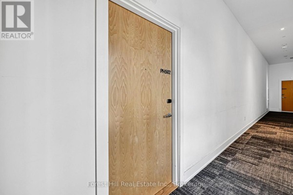 The hallway to apartment PH502 features a light wood door and a patterned carpet. - 502 - 120 Carrick Trail, Gravenhurst)