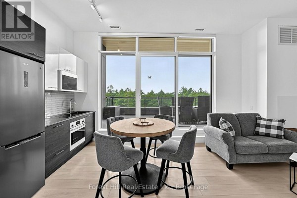 Modern kitchen with stainless steel appliances, dining table, and living area with balcony view. - 502 - 120 Carrick Trail, Gravenhurst)