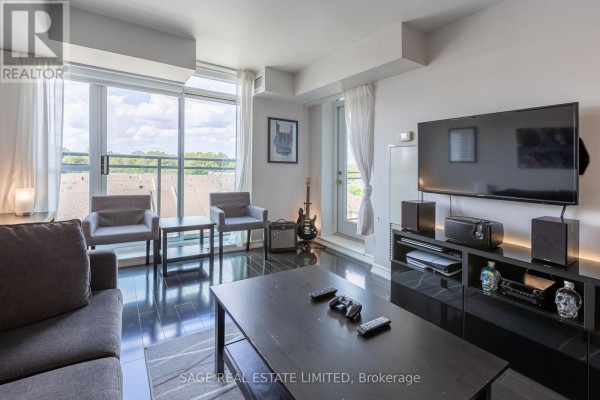 Living room with a sofa, chairs, entertainment unit with TV, and a balcony door. - 502 - 120 Dalliomore Circle, Toronto