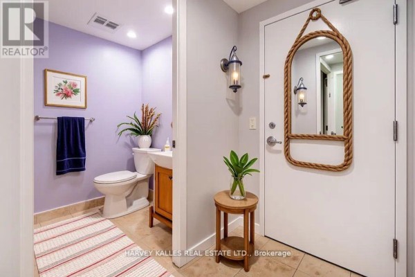 Powder room with a toilet and vanity, next to a mirrored entrance with a small side table. - 502 - 218 Queens Quay W, Toronto