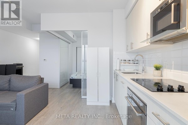 View of apartment living area and kitchen, showing a grey sofa and white cabinets. - 502 - 2550 Simcoe Street N, Oshawa