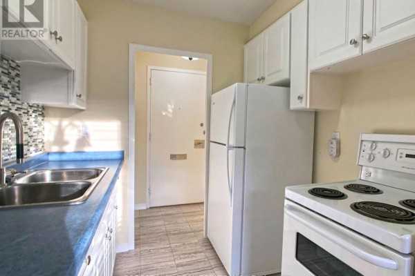 White kitchen cabinets, blue countertop, stainless steel sink, mosaic tile backsplash, white refrigerator, and stove. - 502 - 335 Lonsdale Road, Toronto