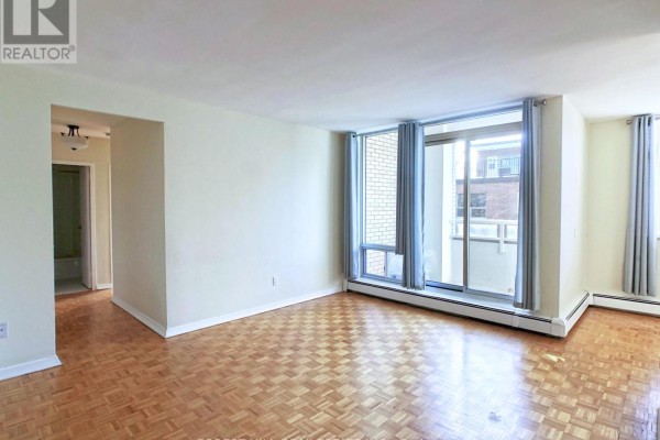 Living room with parquet flooring, large window with sliding glass door to balcony, and gray curtains. - 502 - 335 Lonsdale Road, Toronto