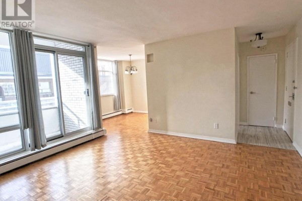 Living room with parquet flooring, large window with sliding glass door, view of balcony, and doorway to hallway. - 502 - 335 Lonsdale Road, Toronto