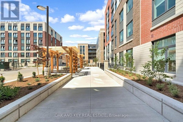 View down a concrete walkway with landscaping and pergolas beside an apartment building. - 502 - 385 Hill Street, London East