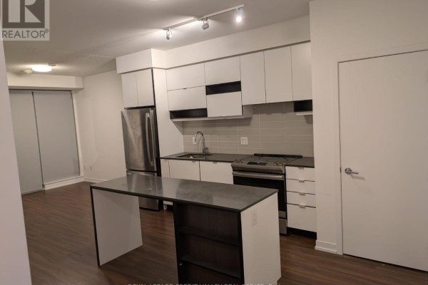 A modern kitchen with white cabinets, stainless steel appliances, a dark island, and grey backsplash. - 502 - 4065 Confederation Parkway, Mississauga