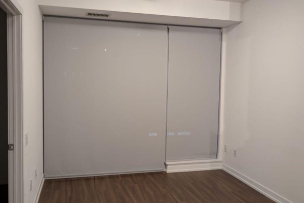 Interior room with two large windows covered by grey roller blinds and dark wood floors. - 502 - 4065 Confederation Parkway, Mississauga