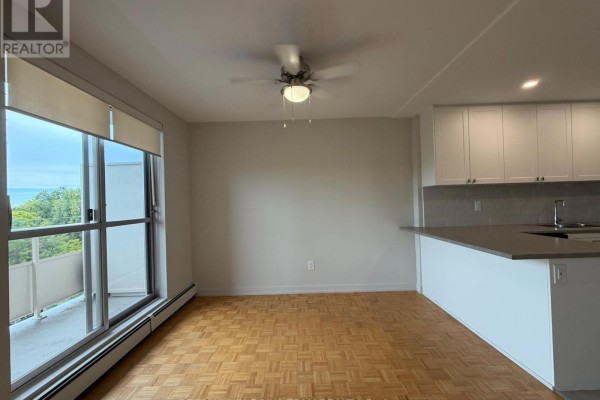 Living and dining area with parquet flooring, beige walls, and a view of trees. - 502 - 60 Windward Street, St  Catharines