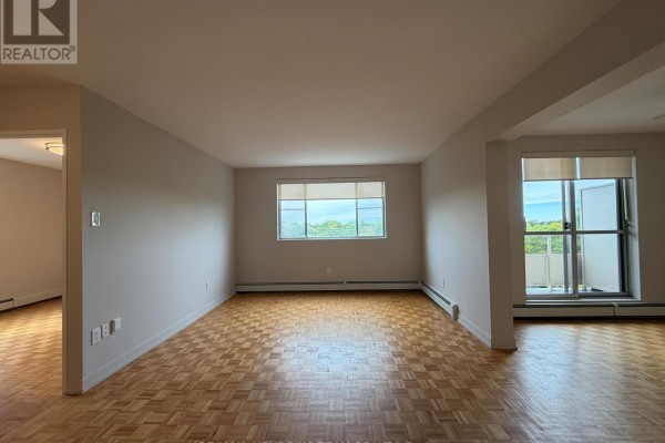 Spacious living room with parquet flooring, beige walls, and access to a balcony. - 502 - 60 Windward Street, St  Catharines