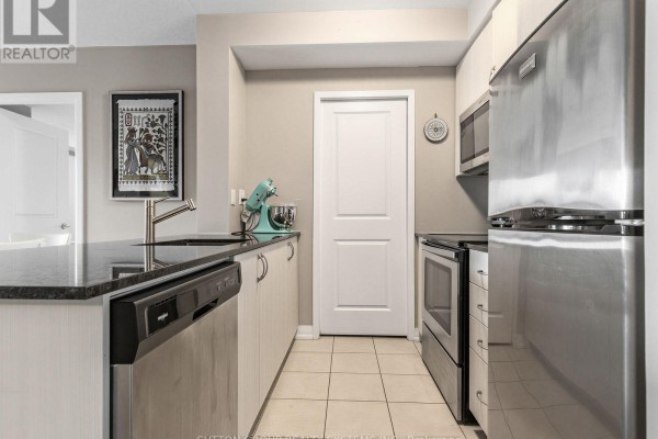 A galley kitchen featuring stainless steel appliances, granite countertops, light wood cabinets, and tiled flooring. - 502 - 741 Sheppard Avenue W, Toronto