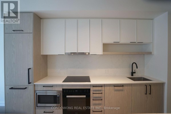 Close-up of modern kitchen with induction stovetop, built-in microwave, and light wood cabinetry. - 502 - 91 Montclair Avenue, Toronto