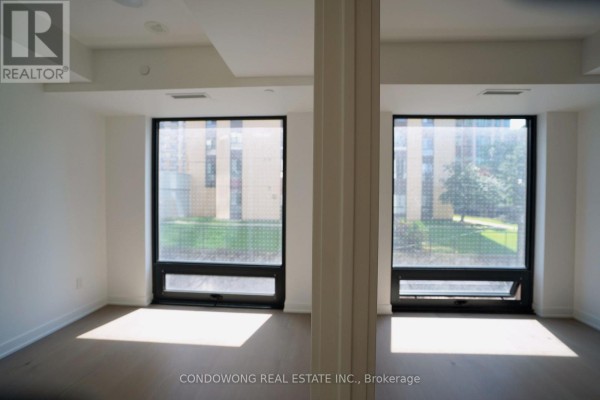 Living area with two large windows showing building views and sunlight streaming onto hardwood floors. - 502 - 91 Montclair Avenue, Toronto
