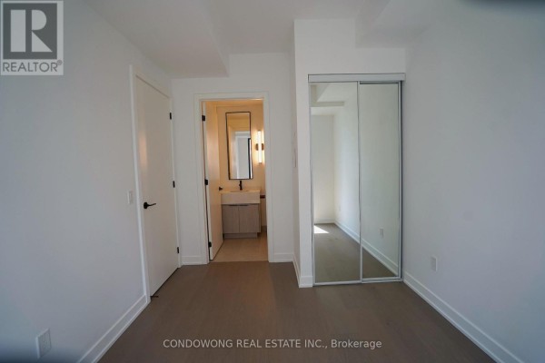 Bedroom with closet and mirrored doors, adjacent to a doorway leading to the bathroom. - 502 - 91 Montclair Avenue, Toronto