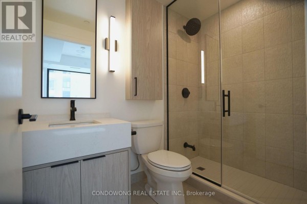 Modern bathroom with a vanity, toilet, and glass-enclosed shower with tiled walls. - 502 - 91 Montclair Avenue, Toronto