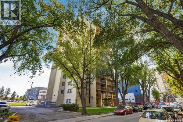 Apartment building exterior with trees and parked cars on street. - 502 430 5th Avenue N, Saskatoon
