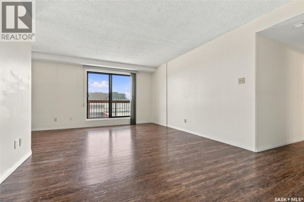 Spacious living room with dark wood floors and a view through window. - 502 430 5th Avenue N, Saskatoon