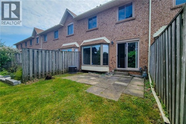 Rear patio with a large propane tank and a folding chair, next to a grassy lawn. - 502 Barton Street Unit# 50, Stoney Creek