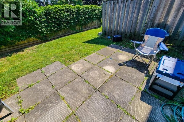 Paved patio area in a fenced backyard with green grass and outdoor seating. - 502 Barton Street Unit# 50, Stoney Creek