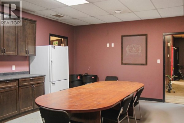 Interior office or break room with a long oval table, chairs, dark wood cabinets, and a white refrigerator. - 5022 50 Avenue, Lougheed