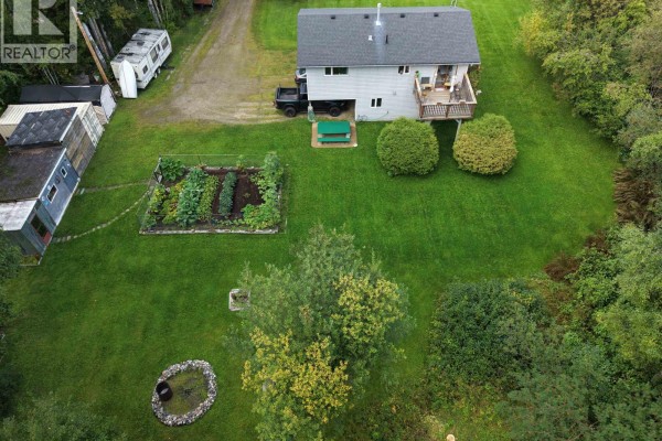 Aerial view showing the house, garden beds, outbuildings, and parked vehicles on the property. - 5027 Sooke Road, Prince George