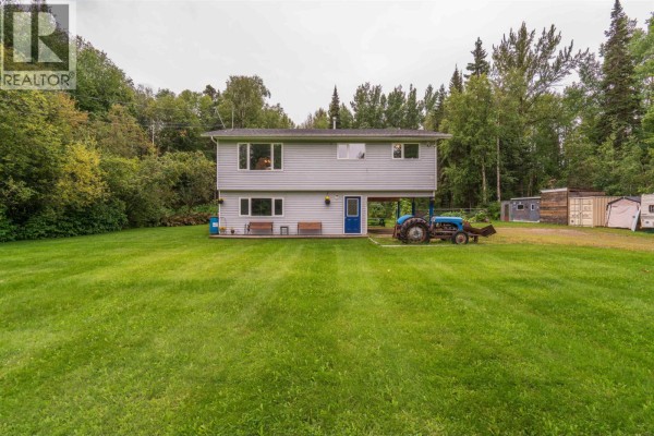 Exterior view of the house from the expansive green lawn, with surrounding forest and outbuildings. - 5027 Sooke Road, Prince George