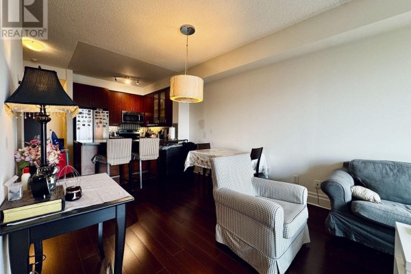 View from living area toward the kitchen, showing dark wood cabinets, stainless steel appliances, and island. - 503 - 111 Upper Duke Crescent, Markham