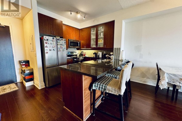 Corner kitchen with dark wood cabinets, granite countertop island, stainless steel appliances, and two bar stools. - 503 - 111 Upper Duke Crescent, Markham