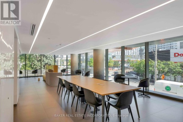 Communal lounge area with long table, chairs, and large windows overlooking the street. - 503 - 28 Eastern Avenue, Toronto