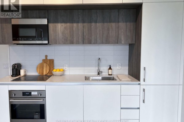 Close-up of modern kitchen cabinetry, stainless steel microwave, tile backsplash, and sink area. - 503 - 322 Dupont Street, Toronto