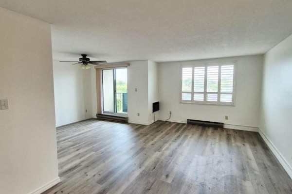 Living room with white plantation shutters on the window and a sliding balcony door. - 503 - 421 Fairview Drive, Brantford