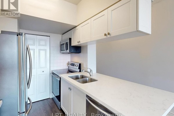 Close-up view of a white kitchen with stainless steel appliances, white countertops, and light wood flooring. - 503 - 8 Hillcrest Avenue, Toronto