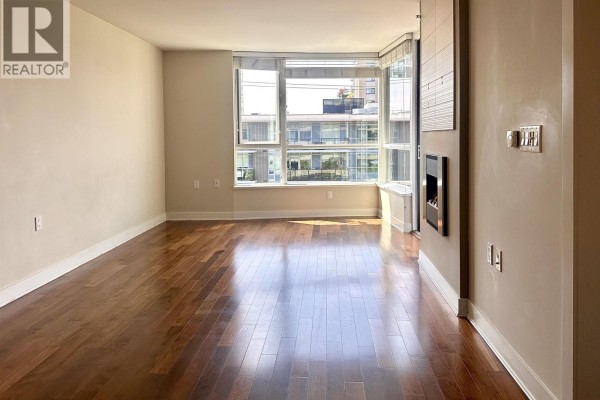 Living room with hardwood floors, large windows, and a gas fireplace. - 503 160 W 3rd Street, North Vancouver